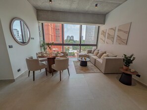 A modern living room with a dining area, large windows, and a view of buildings. - Avmx Living 5A 1 bed (Guadalajara)