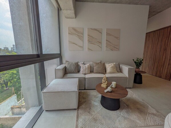 A modern living room with a sofa, ottoman, and coffee table, a large window, and abstract wall art.