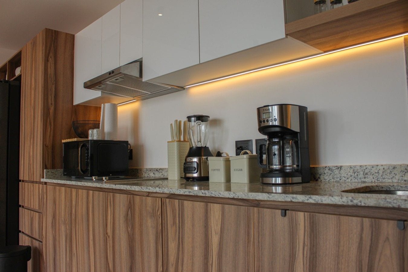 A modern kitchen with wooden cabinets, a built-in microwave, a coffee maker, and a blender on the countertop.