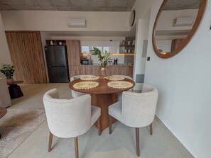 A dining area with a round wooden table, four upholstered chairs, and a vase with a plant. - Avmx Living 5A 1 bed (Guadalajara)
