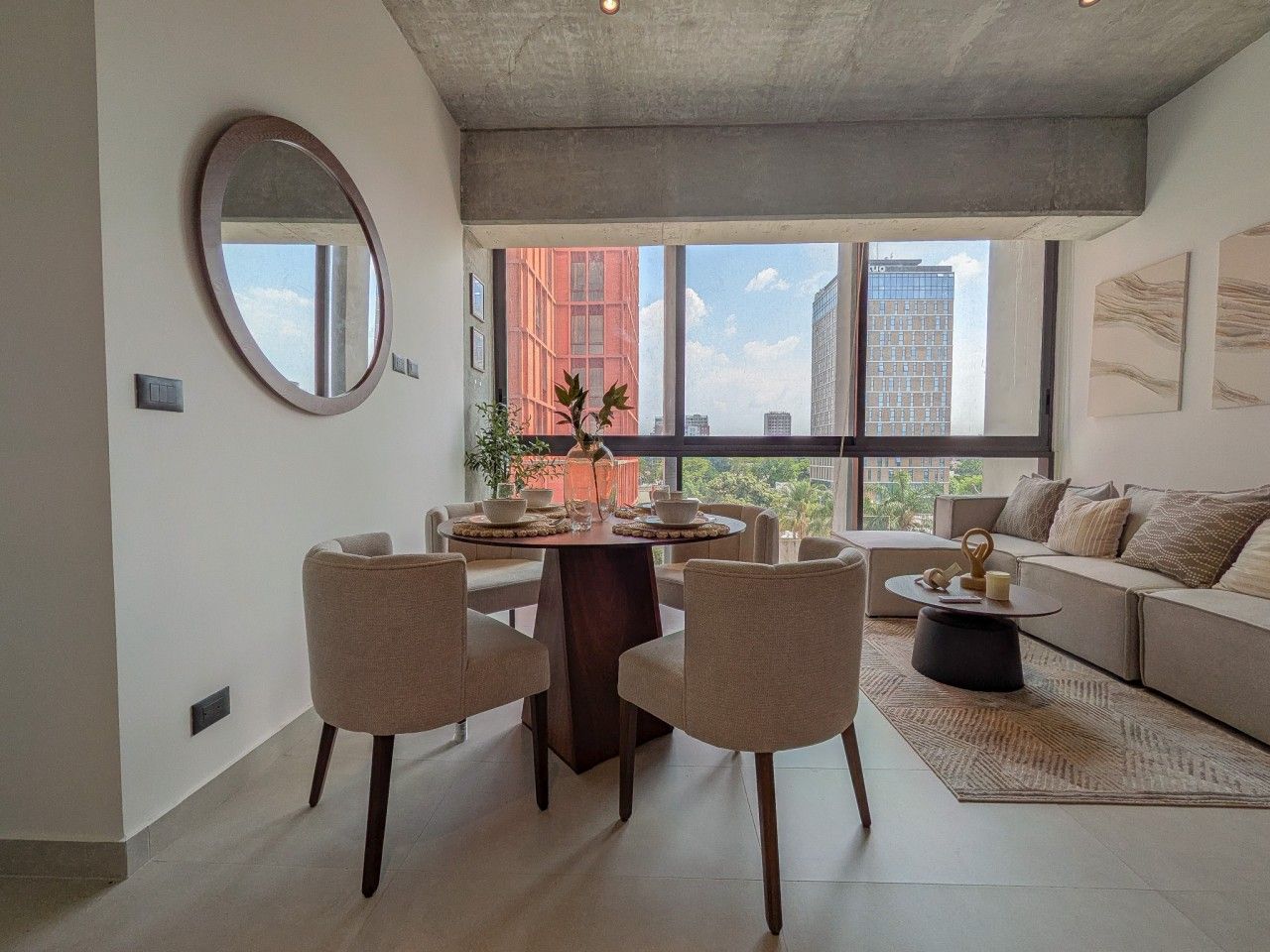 A modern living room with a dining area, large windows, and a view of the city.
