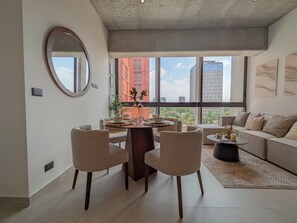 A modern living room with a dining area, large windows, and a view of the city.