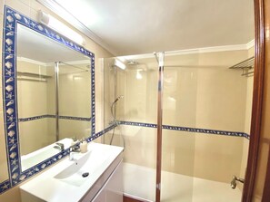 Ein Badezimmer mit einem weißen Waschbecken, einem Spiegel mit blauer Zierleiste und einer Duschkabine aus Glas.
