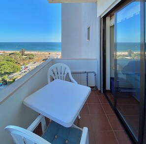 Ein Balkon mit einem weißen Tisch und Stühlen, Blick auf den Strand und einem klaren Himmel.