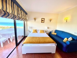 Ein Hotelzimmer mit Bett, einer Couch, einem Balkon mit Tisch und Stühlen sowie Meerblick.