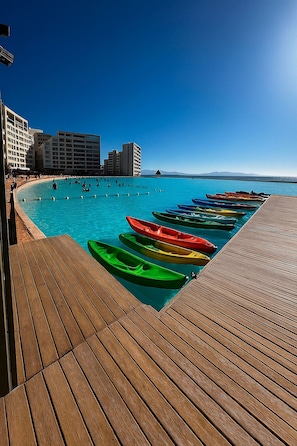 A wooden deck with colorful kayaks lined up, overlooking a clear blue sea with buildings in the background. - Sea, Space and Relaxation – Laguna del Mar (La Serena)