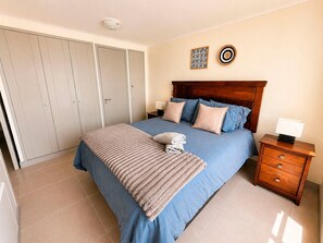 Ein Schlafzimmer mit einem Bett, Nachttischen, einem Kleiderschrank und dekorativen Wandbildern.