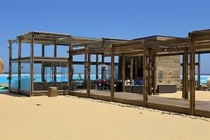 Ein Gebäude am Strand mit Glasfassade, Holzbalken und Sandboden.