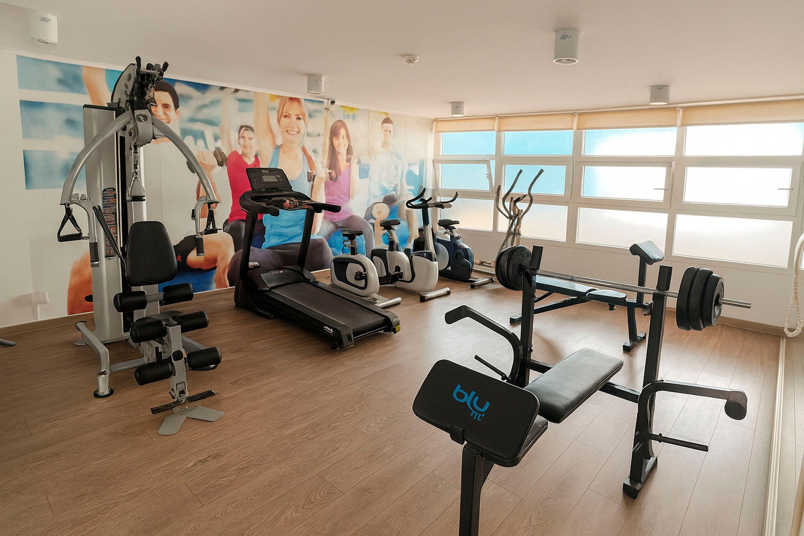 A gym with various exercise equipment, a treadmill, and a wall with a mural.