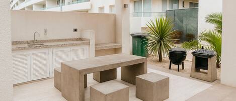 An outdoor patio with a concrete table and benches, a sink, and a barbecue grill.