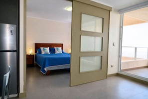Un dormitori amb un llit, una taula de nit, un refrigerador i una porta corredissa de vidre que dona a un balcó.