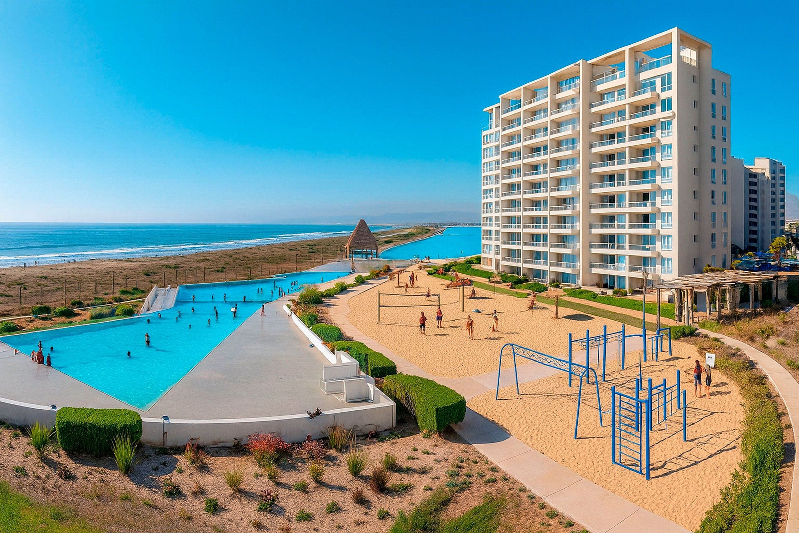 Een kusthotel met een groot zwembadgedeelte, een strand en een hoog gebouw.