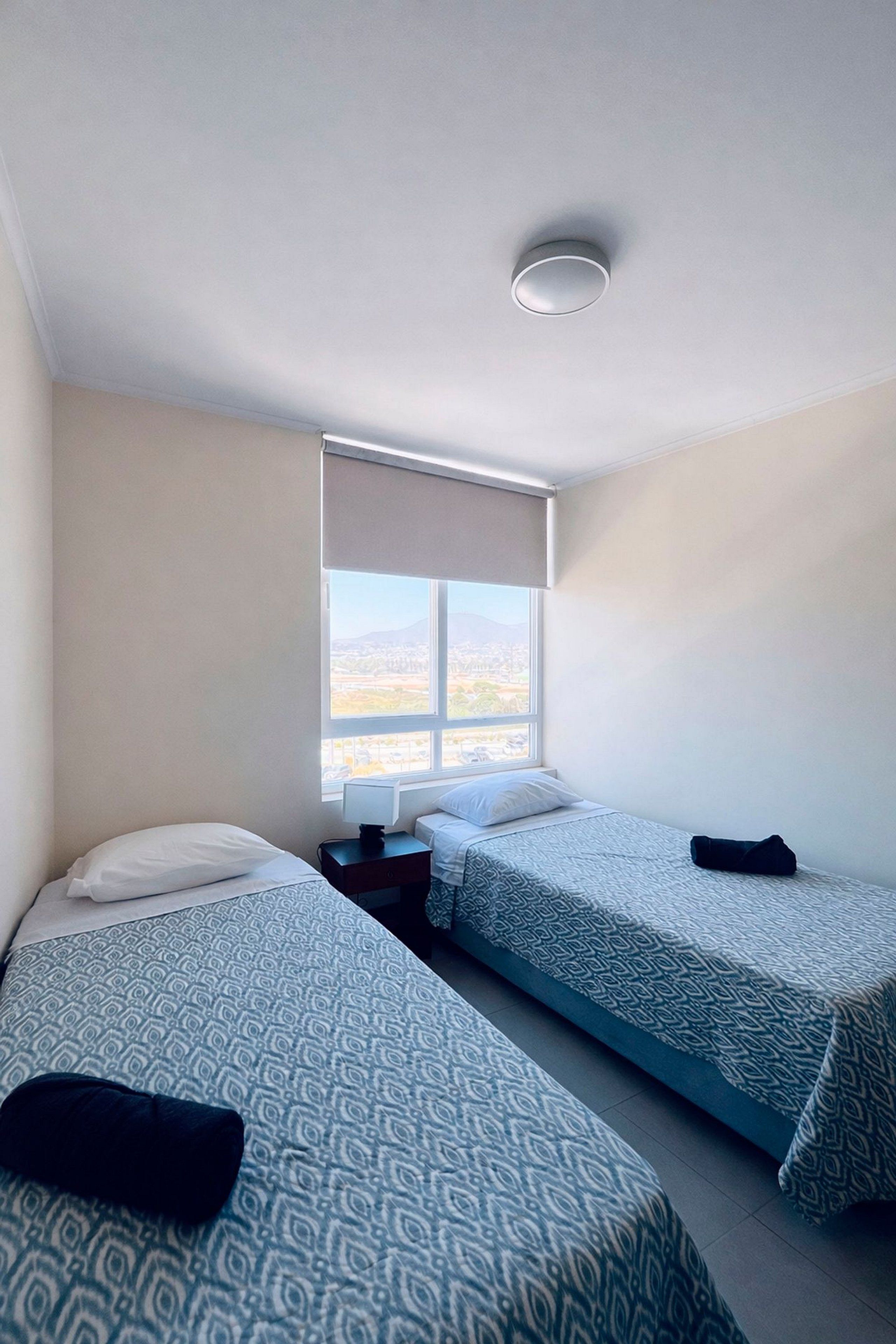 A small, clean room with two beds, a window with a view, and a ceiling light.