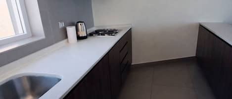 Una cocina con un lavamanos de acero inoxidable, una estufa a gas y armarios de madera oscura.