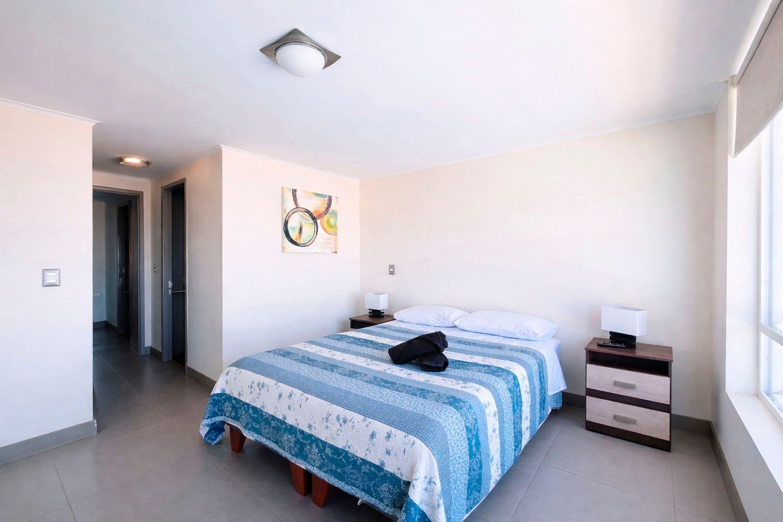 Une chambre d’hôtel avec un lit, une table de chevet, une lampe, un tableau au mur et une fenêtre.
