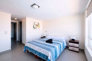 Ein Hotelzimmer mit Bett, Nachttisch, Lampe, einem Gemälde an der Wand und einem Fenster.