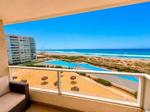 Un balcon avec vue sur une plage, une piscine et un grand immeuble en arrière-plan.
