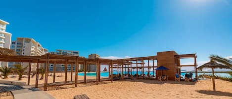 Ein Strand mit Holzkonstruktionen, einem Pool und Blick auf den Ozean.