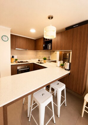 Eine moderne Küche mit Kochinsel, Holzschränken, Backofen, Mikrowelle und einem Edelstahl-Kühlschrank.