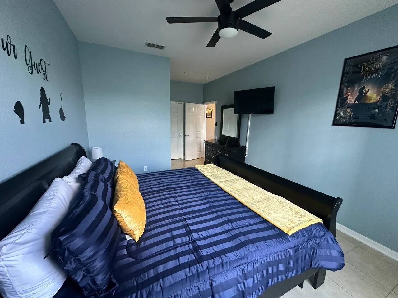 A bedroom with a bed, a ceiling fan, a wall with silhouettes, a door, a dresser, and a poster.