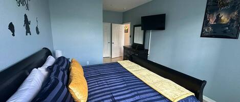 A bedroom with a bed, a ceiling fan, a wall with silhouettes, a door, a dresser, and a poster.