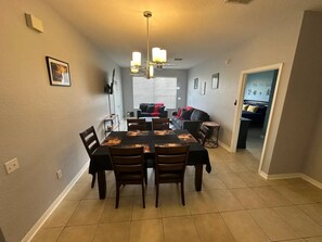 A dining area with a rectangular table, chairs, and a chandelier. - Disney Escape at Windsor Palms (Kissimmee)