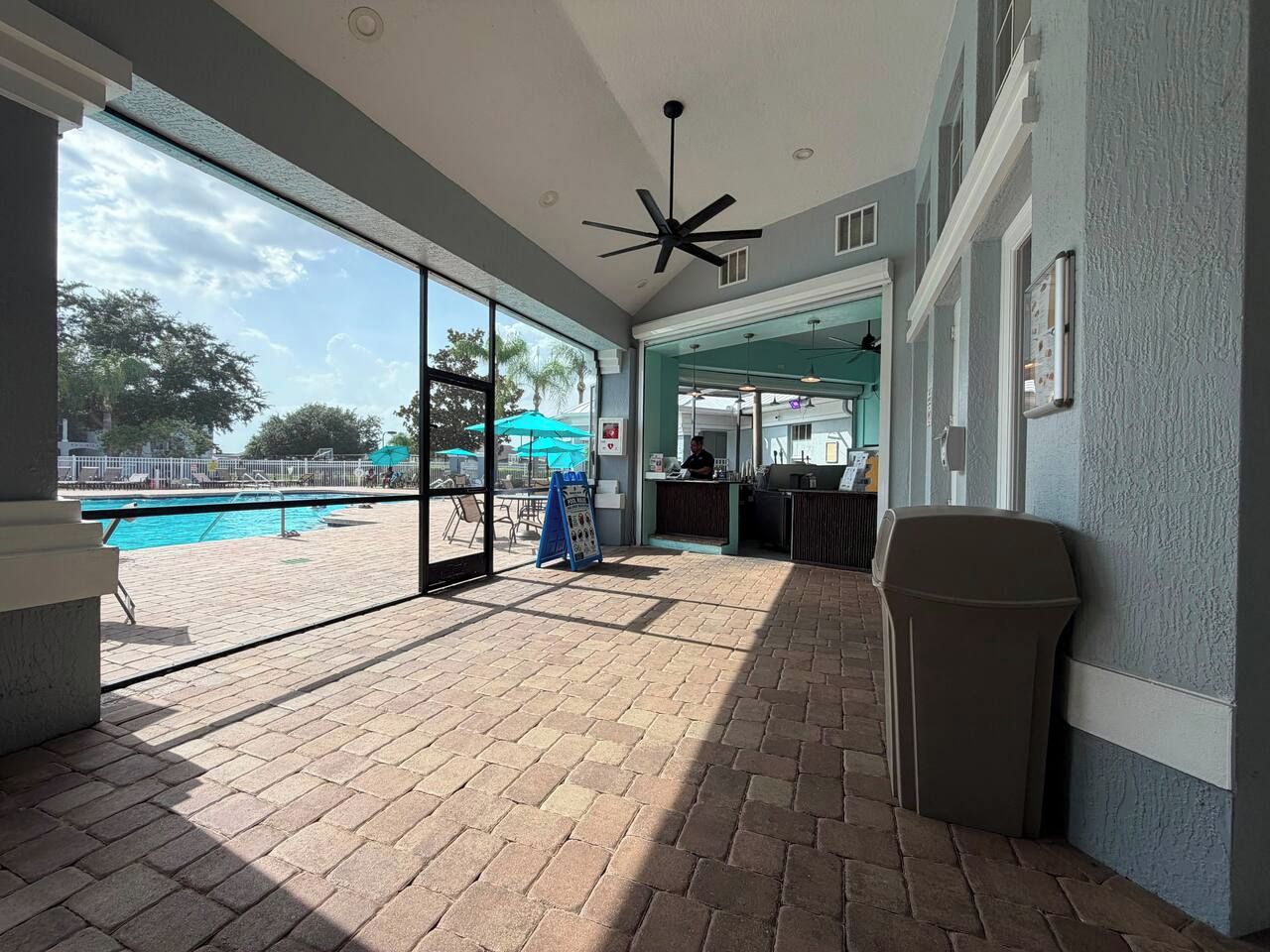 An indoor pool area with a brick floor, a ceiling fan, and a view of the outdoor swimming pool.