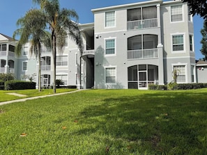 A multi-story residential building with balconies, a well-maintained lawn, and a clear sky. - Disney Escape at Windsor Palms (Kissimmee)