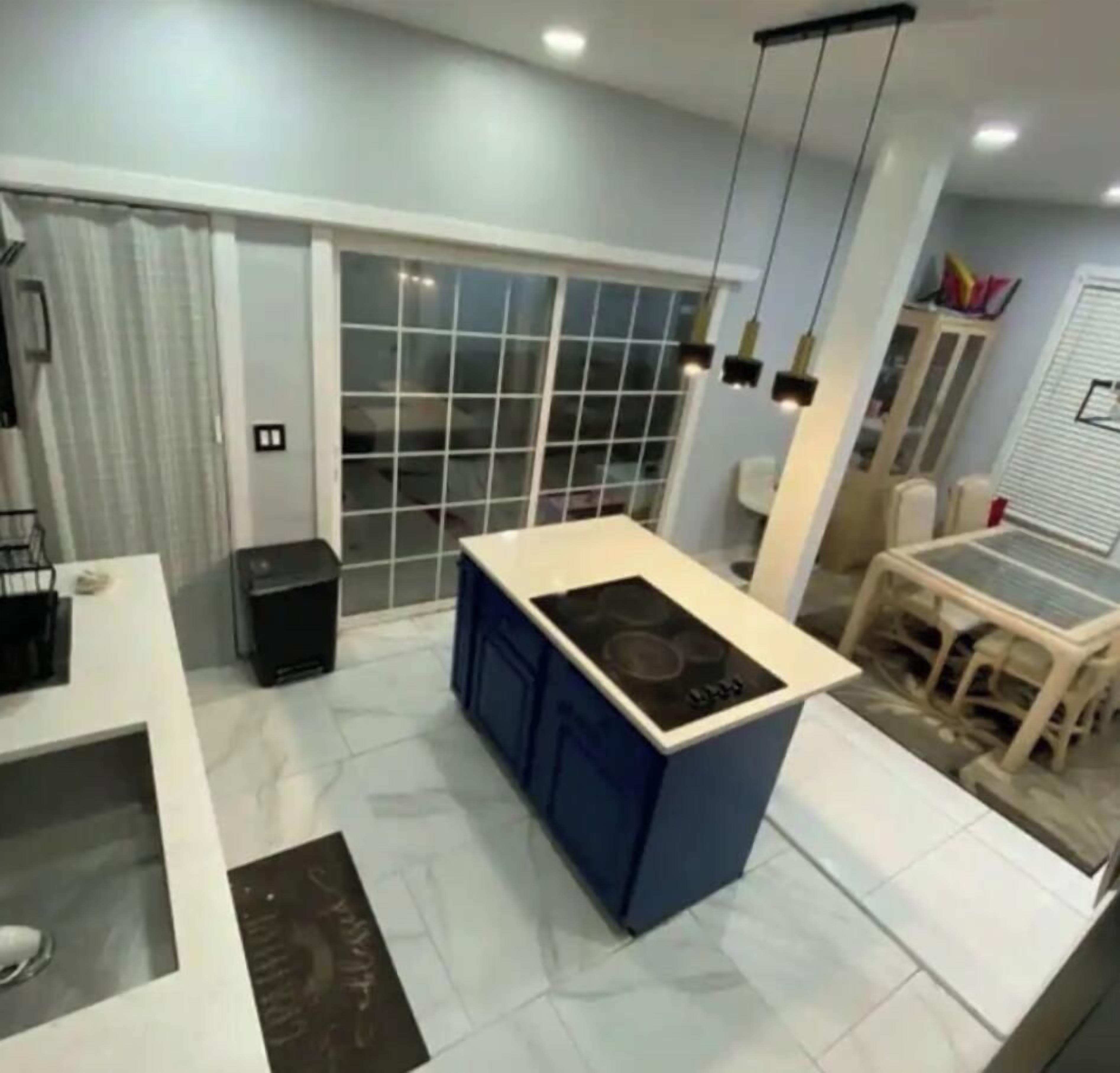 Una cocina moderna con una isla central, una zona de comedor con mesa y sillas, y un puerta corrediza de vidrio que da a un balcón.