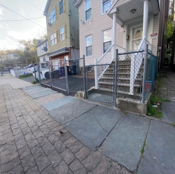 A residential building with a front porch, a staircase, and a fenced driveway.