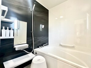 A modern bathroom with a dark wood vanity, a white bathtub, and a shower. - Vrbo Property (うるま市)