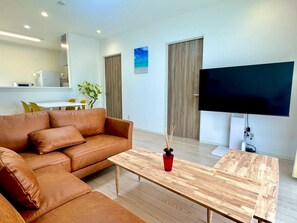 A modern living room with a leather sofa, a wooden coffee table, and a flat-screen TV. - Vrbo Property (うるま市)
