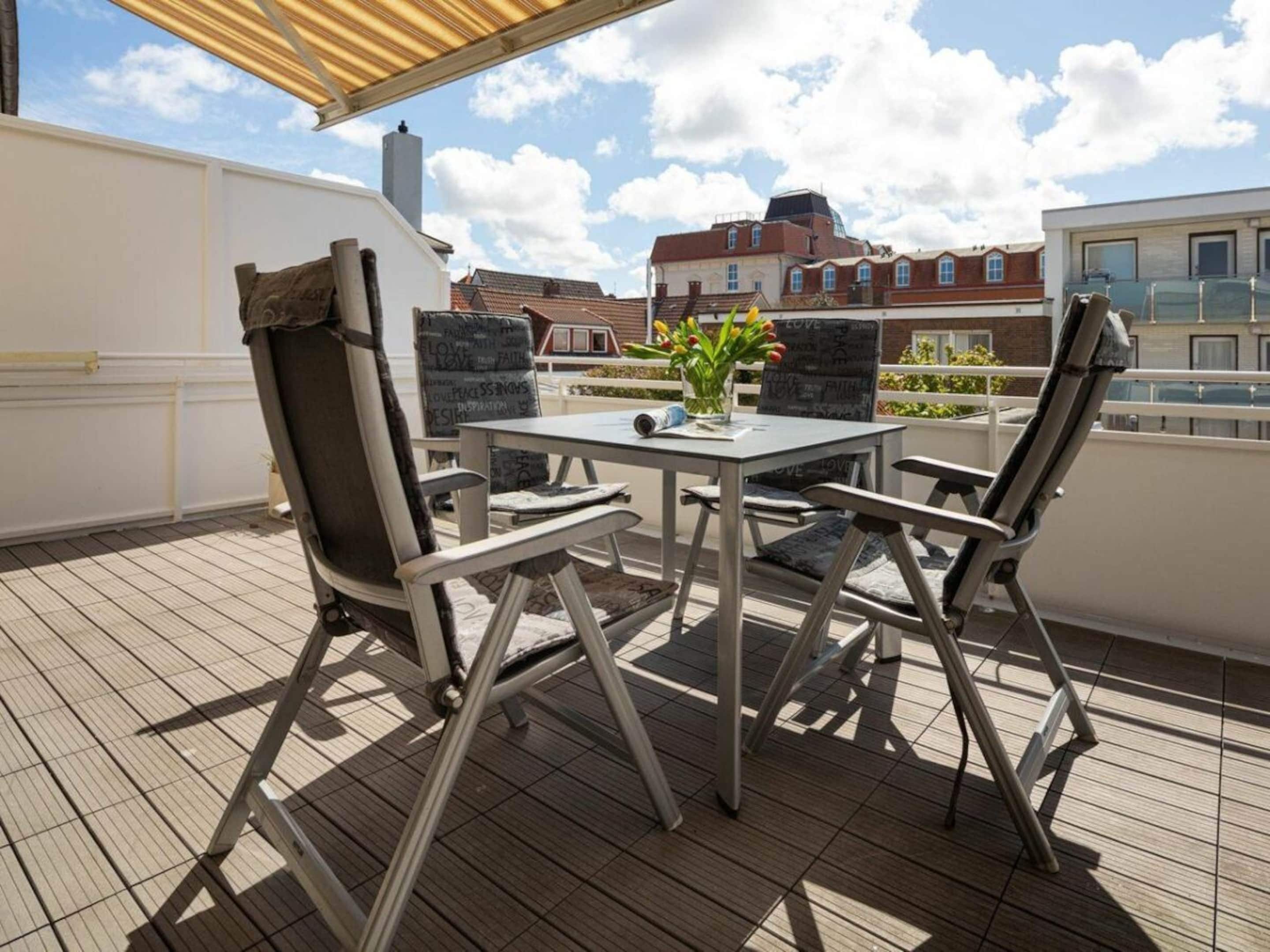 Een terras op het dak met een tafel, stoelen, een bloempot en een uitzicht op gebouwen.