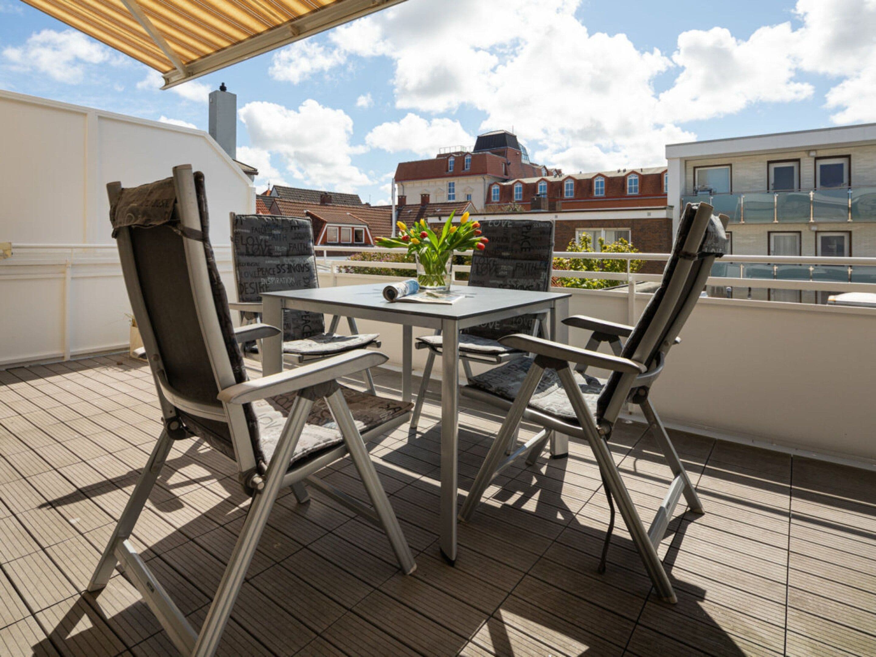 An outdoor seating area with a table and chairs, a potted plant, and a view of buildings in the background.
