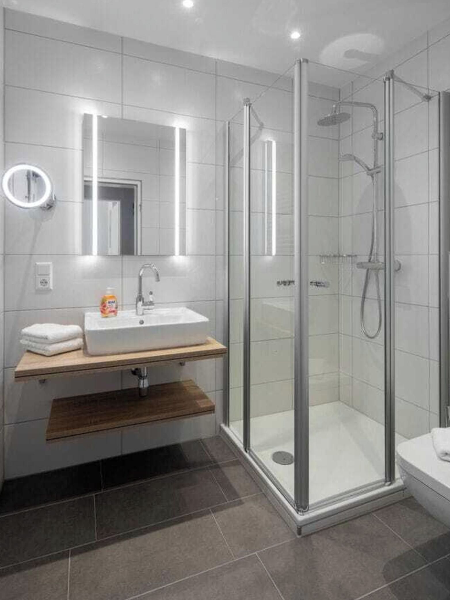 Un bany modern amb dutxa de vidre, un lavabo blanc i un mirall amb llum.