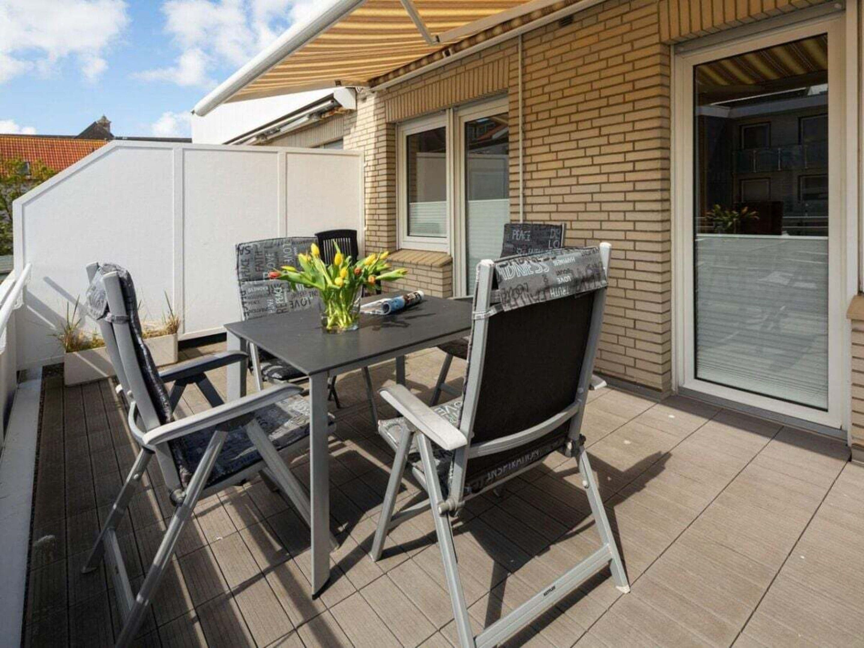 Una terrazza esterna con tavolo e sedie, un piccolo giardino e un edificio con facciata in mattoni e ampie finestre.