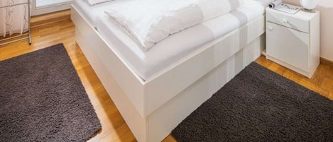 A bedroom with a bed, a nightstand, a radiator, a window, and a picture on the wall.
