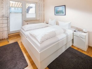 A bedroom with a bed, a nightstand, a radiator, a window, and a picture on the wall. - Holiday Apartment in Norderney With Wi-fi (Norderney)