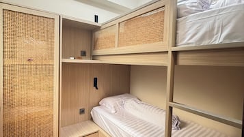A bunk bed room with a rattan partition, a small shelf, and a ceiling light.