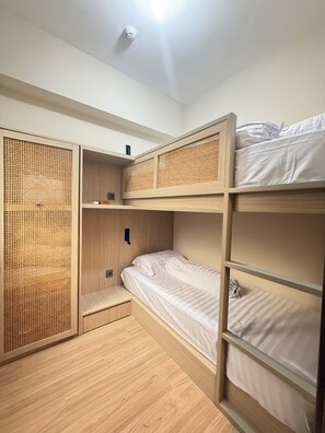 Ett rum med en våningssäng, en avskärmning av rotting, en liten hylla och en taklampa.