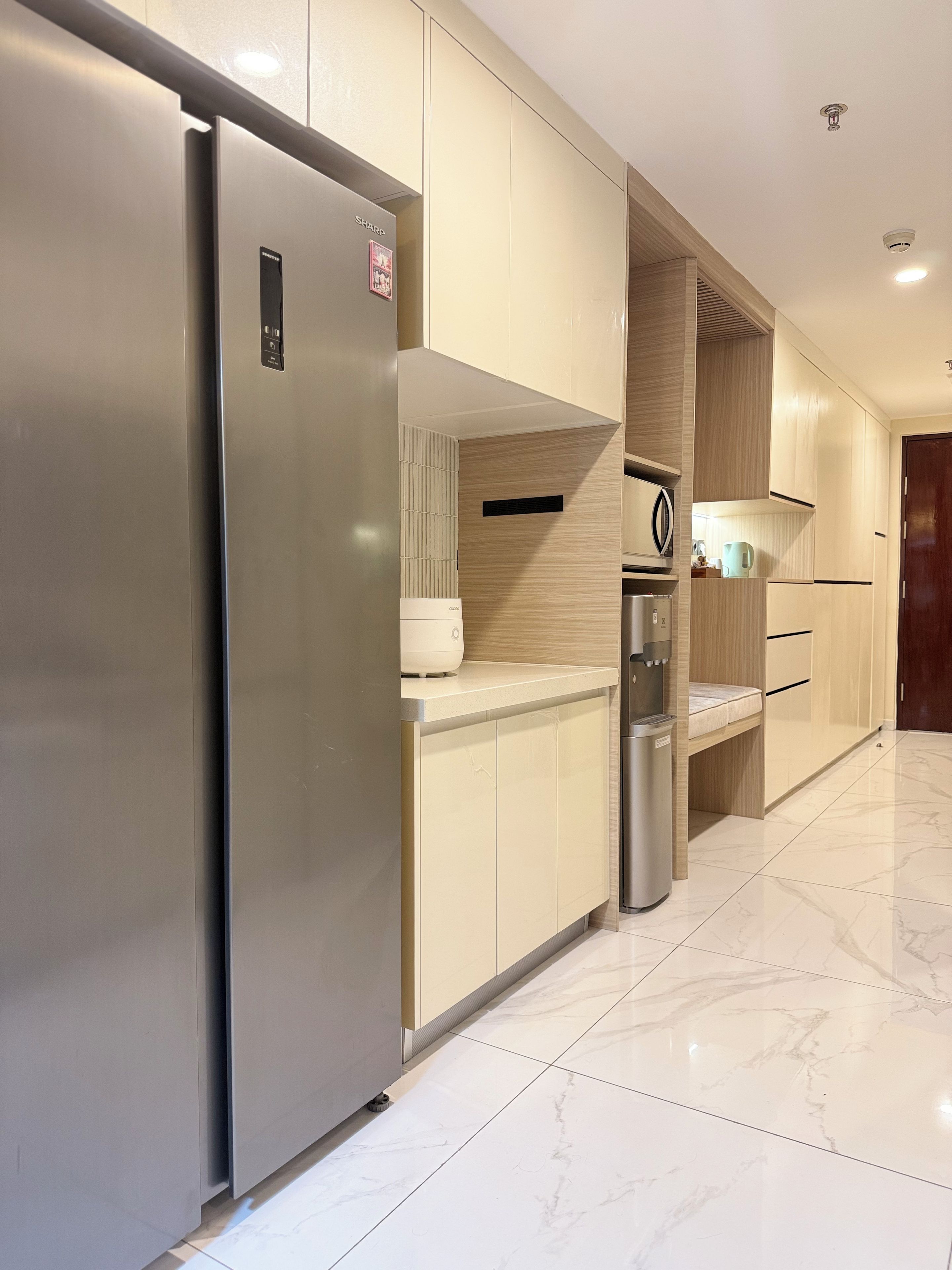 A modern kitchen with a stainless steel refrigerator, wooden cabinets, and a marble floor.