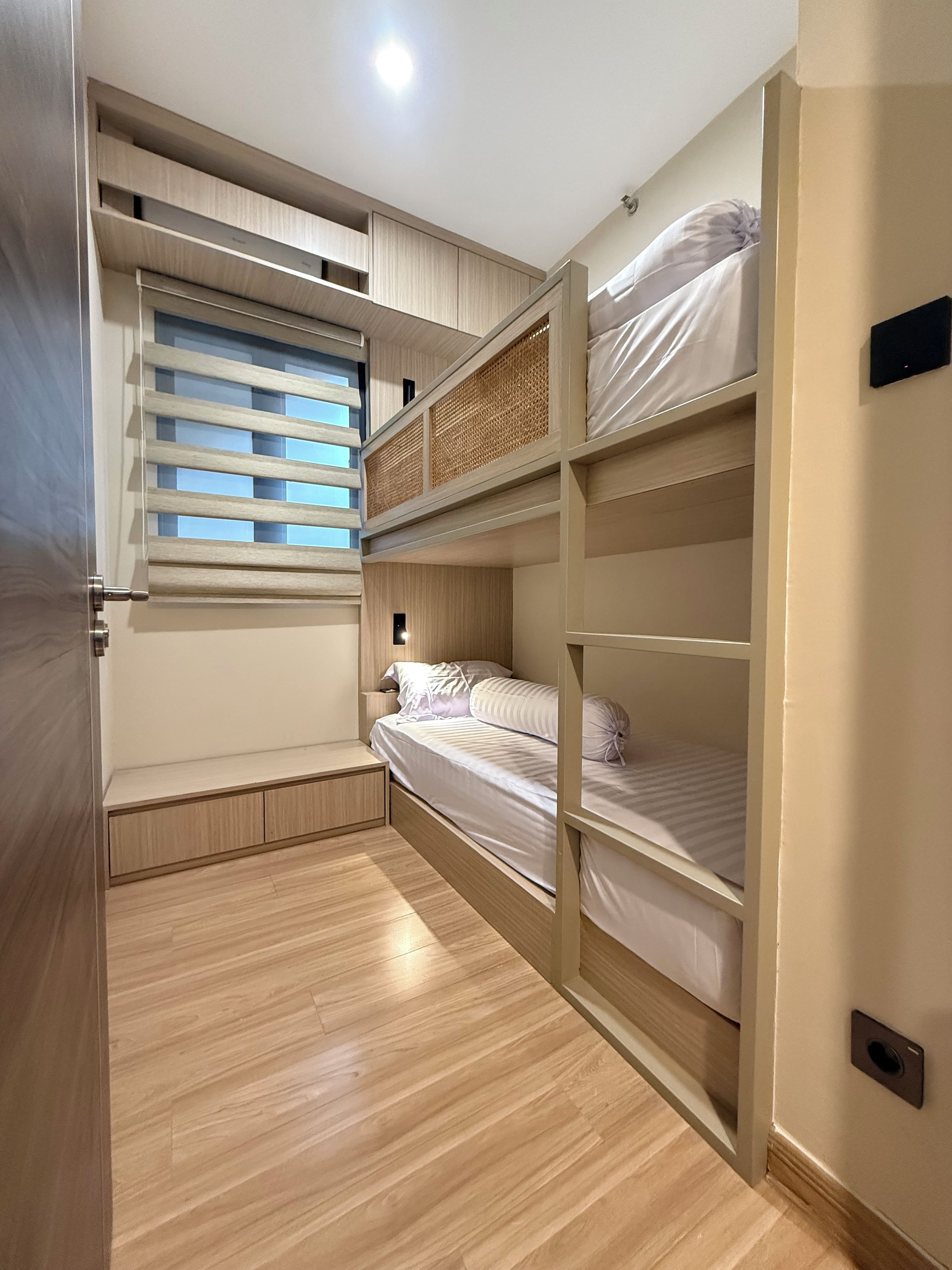 A bedroom with a bunk bed, built-in shelving, and a window with blinds.