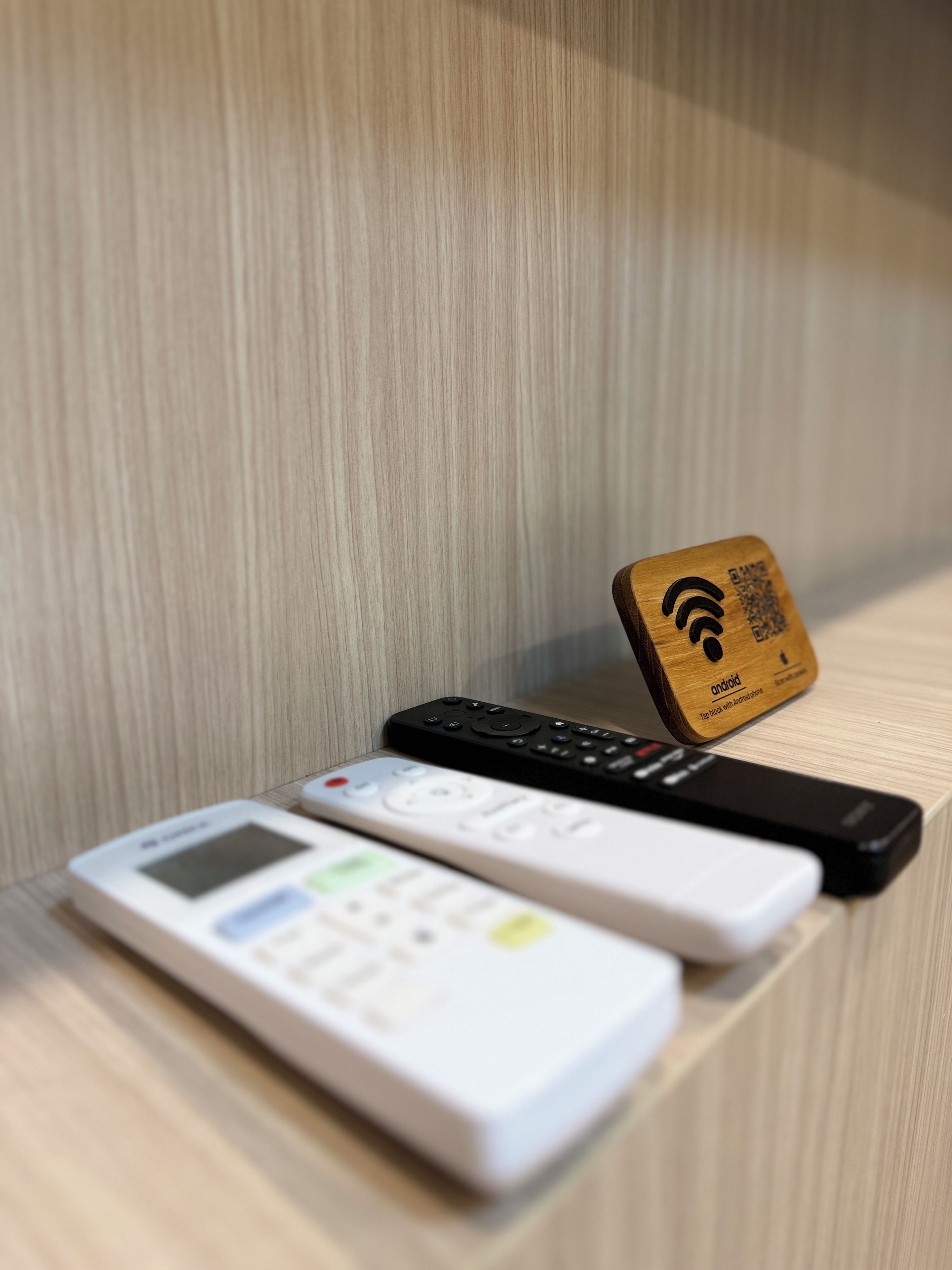 Un estante de madera con un control remoto, un teléfono inteligente y una etiqueta con un código QR.