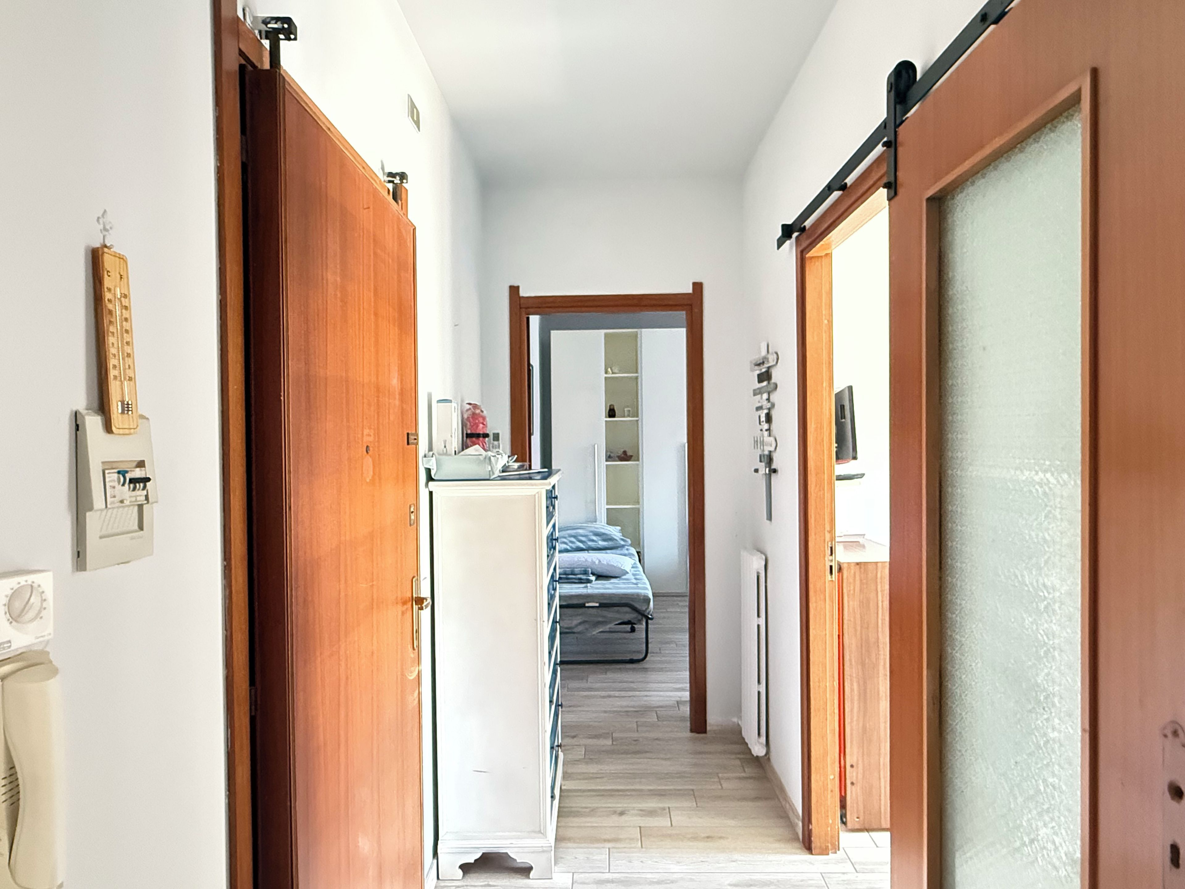 Un couloir étroit, avec des portes en bois de chaque côté, qui mène à une pièce contenant un lit et un radiateur.
