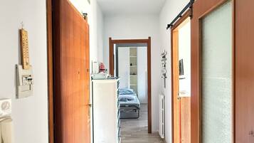 Un couloir étroit, avec des portes en bois de chaque côté, qui mène à une pièce contenant un lit et un radiateur.
