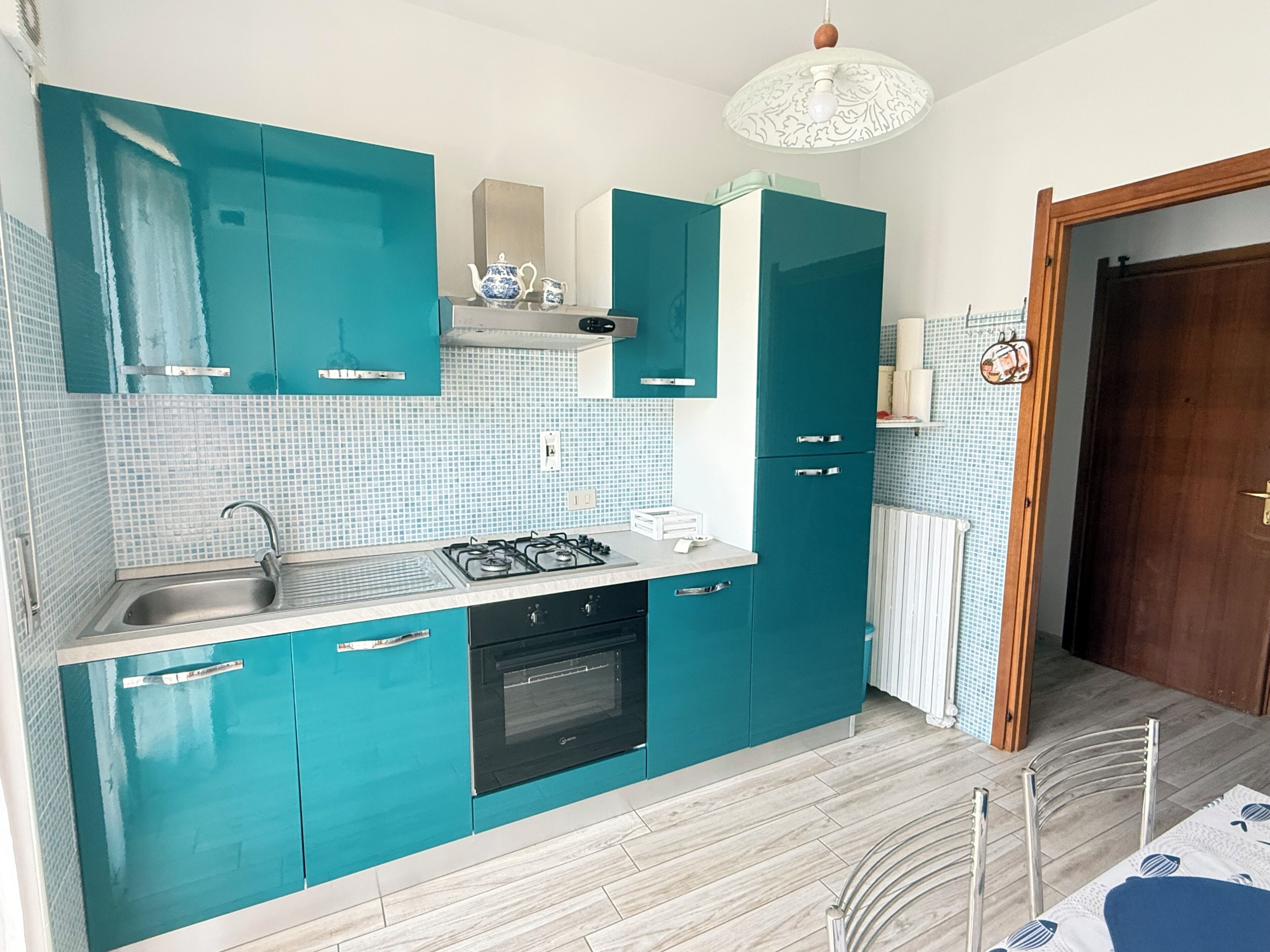 Una cucina compatta con mobili color petrolio, un piano cottura a gas e un forno integrato.