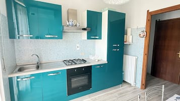 Una cucina compatta con mobili color petrolio, un piano cottura a gas e un forno integrato.
