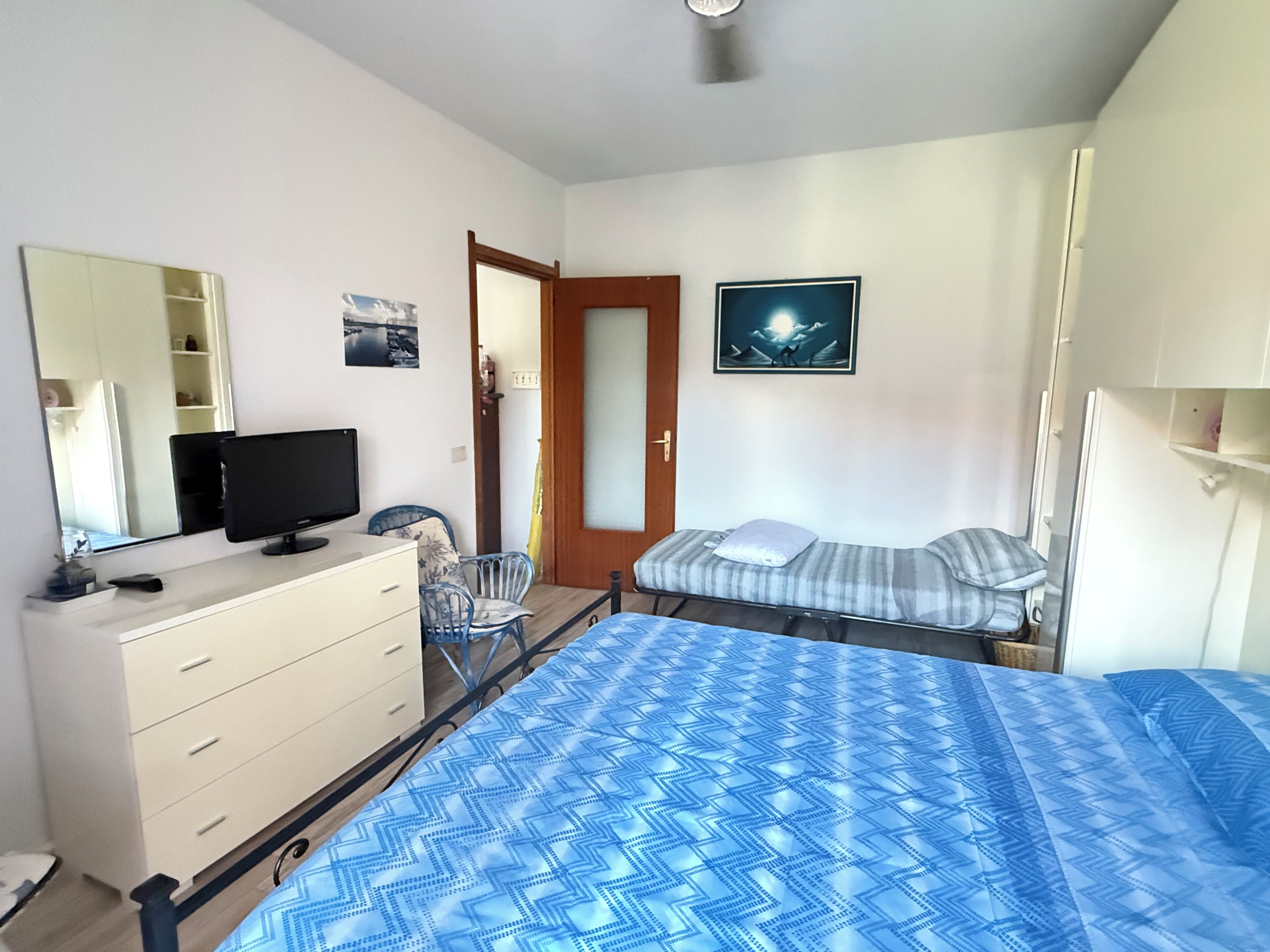 Una camera da letto con un letto, una cassettiera, una televisione, una sedia e una porta.
