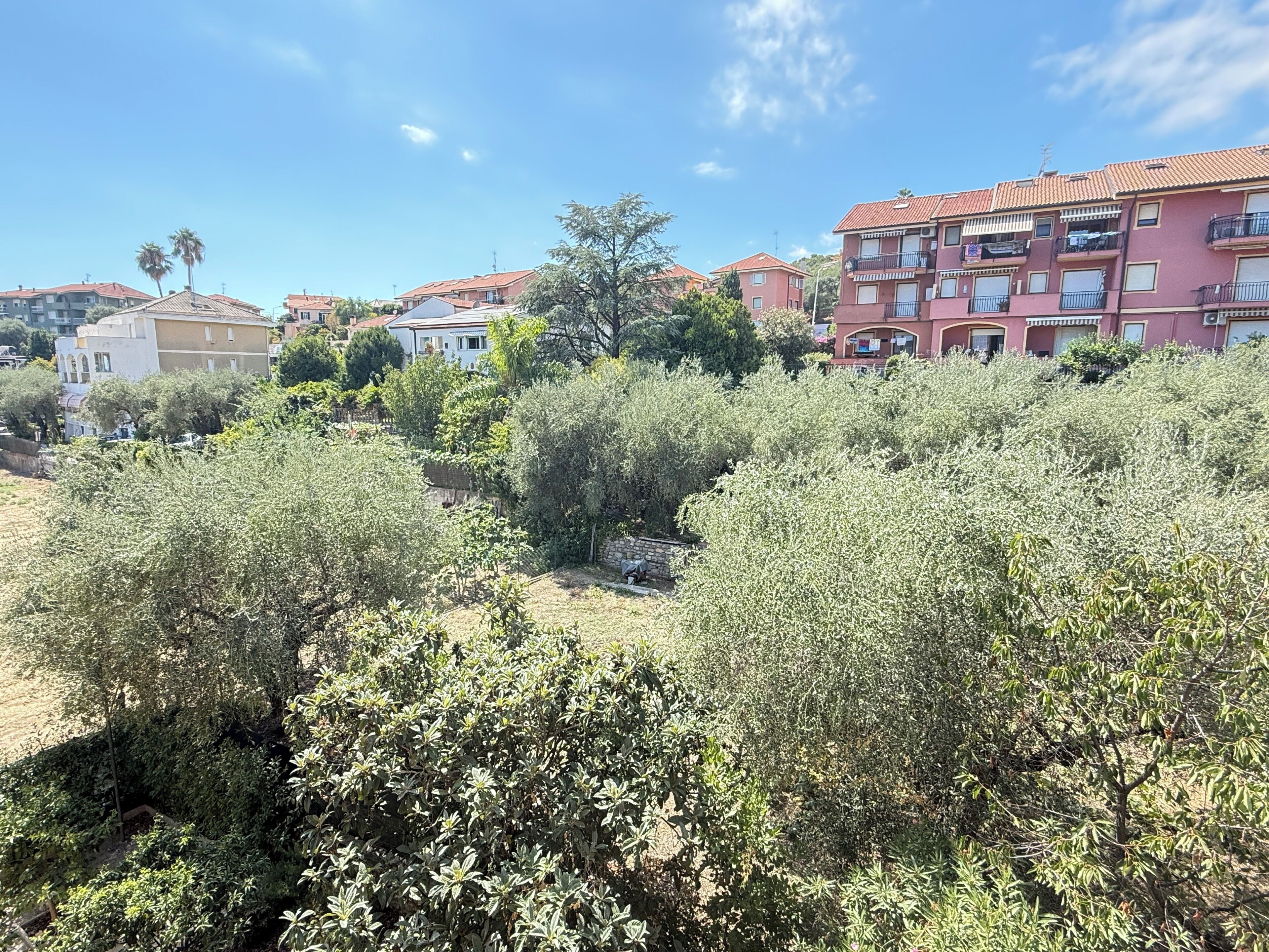 A residential area with multi-story buildings, dense shrubbery, and a clear sky.