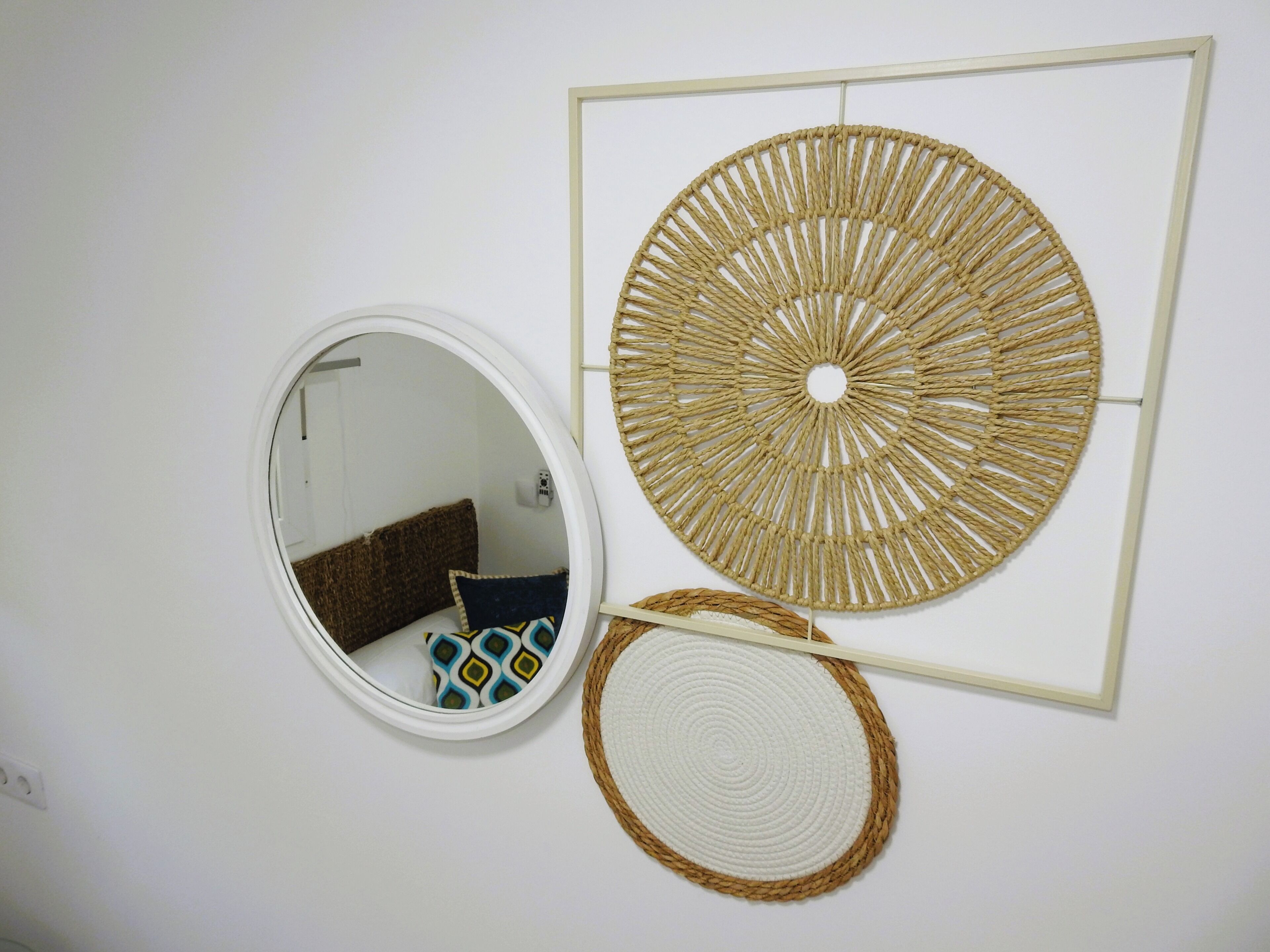A wall with a circular mirror, a woven wall art piece, and a woven placemat.